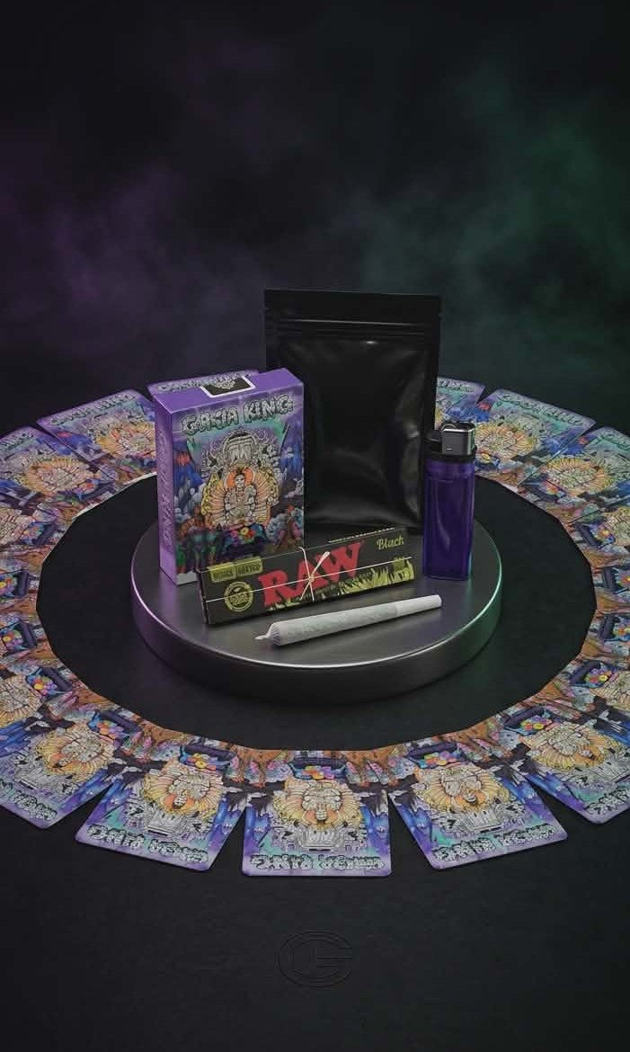 Collection of ganja ring card game items including cards, a box, and a tube on a dark surface with a mystical background.