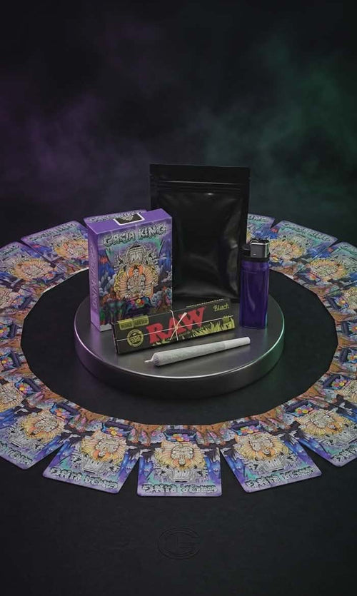 Collection of ganja ring card game items including cards, a box, and a tube on a dark surface with a mystical background.